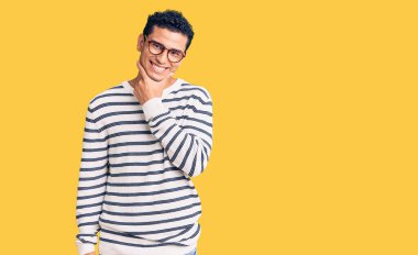 İspanyol asıllı yakışıklı genç adam gündelik kıyafetler ve gözlük takıyor kameraya kendinden emin bakıyor kollarını kavuşturup ve çenesini kaldırarak gülümsüyor. Olumlu düşünmek. 