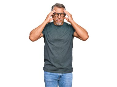 Orta yaşlı, gri saçlı, günlük kıyafetler ve gözlük takan baş ağrısı çeken çaresiz ve stresli bir adam. Çünkü ağrı ve migren. Eller başının üstünde.. 