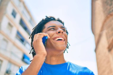 Genç Afrikalı Amerikalı gülümseyen mutlu bir adam şehrin caddesinde akıllı telefondan konuşuyor..