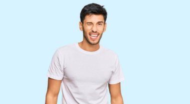 Gündelik beyaz tişört giyen genç yakışıklı adam kameraya seksi bir ifadeyle bakıyor, neşeli ve mutlu bir yüzle.. 