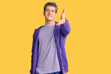 Hoş geldin demek ve karşılamak için gülümseyen mor bir kazak giyen genç yakışıklı bir adam. başarılı iş. 