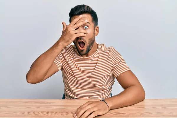 Bonito Hispânico Vestindo Roupas Casuais Sentado Mesa Espreitando Choque Cobrindo — Fotografia de Stock