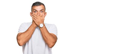 Sıradan beyaz tişört giyen orta yaşlı yakışıklı bir adam yanlışlıkla elleriyle ağzını kapatırken şok oldu. gizli kavram. 