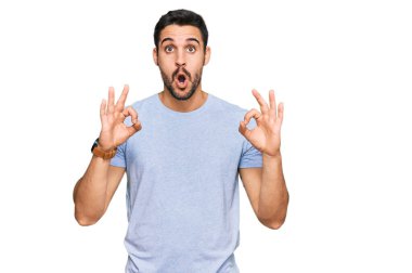 Gündelik kıyafetler giyen genç İspanyol adam şaşırmış ve şok olmuş görünüyor. Tamam sembolünü parmaklarıyla yapıyor. çılgın ifade 