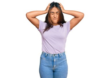 Genç Latin kadın gündelik kıyafetler giyiyor. Baş ağrısı, acı ve migren yüzünden çaresiz ve stresli. Eller başının üstünde.. 