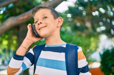 Sevimli beyaz çocuk gülümsüyor. Parktaki akıllı telefondan konuşuyor..