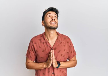 Yaz kıyafetleri giyen genç yakışıklı adam elleri bağlı yalvaran ve dua eden yüzünde umut ifadesi olan çok duygusal ve endişeli bir adam. Yalvarıyor. 