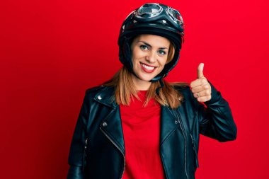 Motosiklet kaskı takan, mutlu ve pozitif gülümseyen, mükemmel ve onay işareti yapan İspanyol genç bir kadın. 