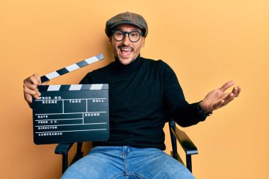 Dövmeli yakışıklı adam elinde video film klasörü ile yönetmen koltuğunda oturmuş başarıyı mutlu bir gülümsemeyle ve kazanan yüz ifadesiyle kutluyor. 