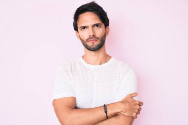 Yakışıklı, beyaz tişört giyen, kuşkucu ve gergin, yüzünde çapraz kollu tasvip etmeyen bir İspanyol. negatif kişi. 