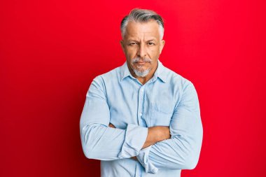 Orta yaşlı, gri saçlı, sıradan kıyafetler giyen şüpheci ve gergin, yüzünde çapraz kollu tasvip etmeyen bir ifade. negatif kişi. 