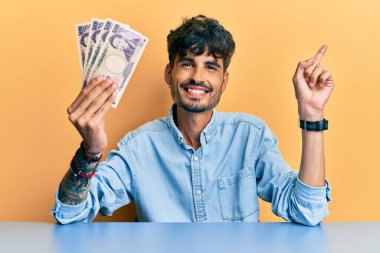 Japon yen banknotları tutan İspanyol genç adam masaya oturmuş gülümsüyor mutlu bir şekilde elini ve parmağını yana doğru uzatıyordu. 