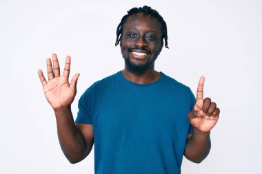 Saçları örgülü genç Afro-Amerikalı adam altı numarayı gösterip gösterirken kendinden emin ve mutlu gülümsüyor.. 