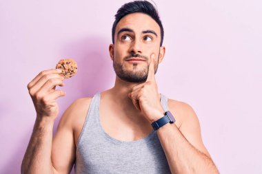 Sakallı, kolsuz tişörtlü, çikolatalı kurabiye yiyen, ciddi yüzlü, eli çenesinde soru soran, kafa karıştırıcı bir adam.