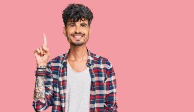 Gündelik kıyafetler giyen genç İspanyol bir numarayı gösterip işaret ederken kendinden emin ve mutlu bir şekilde gülümsüyor.. 