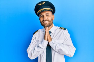 Sakallı, uçak pilotu üniforması giyen, elleri birarada dua eden, affedilmek isteyen, kendine güvenen yakışıklı bir adam.. 