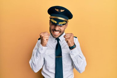 Başarılı olmak için heyecanlanan, kollarını kaldırmış ve gözleri kapalı zaferi kutlayan yakışıklı İspanyol pilot üniforması giyiyor. Kazanan konsept. 