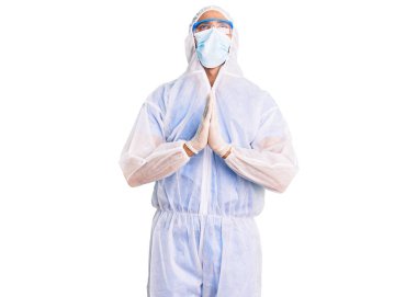 Doktor koruması Coronavirus üniforması giyen genç İspanyol adam ve tıbbi maske. Yüzünde umut ifadesi olan ve endişeli bir şekilde el ele yalvarıp dua eden genç adam. Yalvarıyor. 