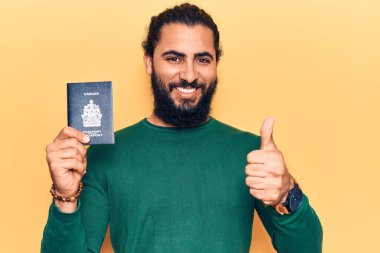Kanada pasaportu taşıyan genç Arap adam mutlu ve pozitif gülümsüyor, başparmağıyla mükemmel ve onay işareti yapıyor. 