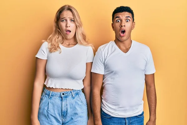 Young Interracial Couple Wearing Casual White Tshirt Afraid Shocked Surprise — Stock fotografie