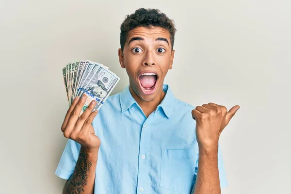 Joven Hombre Afroamericano Guapo Sosteniendo Dólares Apuntando Pulgar Hacia Lado —  Fotos de Stock