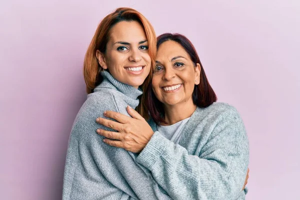 西班牙裔母亲和女儿高兴地微笑着 拥抱着孤零零的粉红背景 — 图库照片