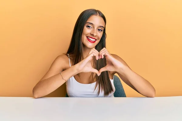Jonge Spaanse Vrouw Casual Kleding Zittend Tafel Glimlachend Liefde Hartsymbool — Stockfoto