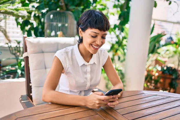 スマホを使って晴れた日にテラスに座って短い髪の美しい女性 — ストック写真