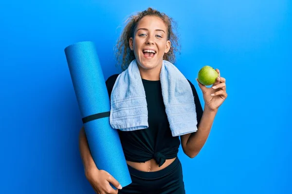 美丽的高加索少女 拿着瑜伽垫和青苹果笑着大声笑着 因为有趣的疯狂笑话 — 图库照片