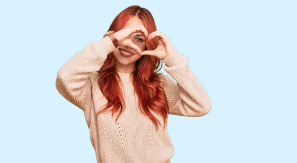 年轻的红头发女人穿着宽松的冬季毛衣 手和手指微笑着做着心脏的形状 透过标志看过去 — 图库照片