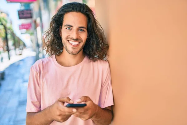 若いヒスパニック系の男笑顔幸せな使用してスマートフォンの壁にもたれて — ストック写真