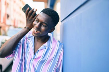 Genç Afrikalı Amerikalı gülümseyen adam şehrin caddesindeki akıllı telefonda mutlu bir şekilde konuşuyor..