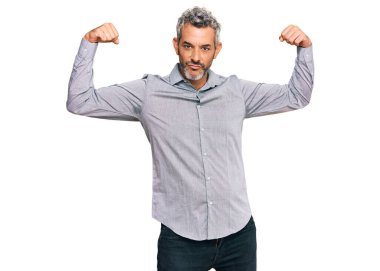 Orta yaşlı, gri saçlı, sıradan kıyafetler giyen, gururla gülümseyen kol kaslarını gösteren bir adam. fitness konsepti. 