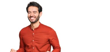 Gündelik kıyafetler giyen genç İspanyol adam çok mutlu ve heyecanlı. Kazanan jestler yapıyor. Kolları havada, gülümsüyor ve başarı için bağırıyor. kutlama konsepti. 