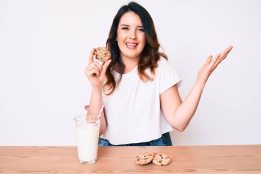 Genç, güzel esmer kadın bir bardak taze süt içiyor. Kurabiyelerle zaferi kutluyor. Gülümsüyor ve ellerini kaldırarak kazanıyor. 