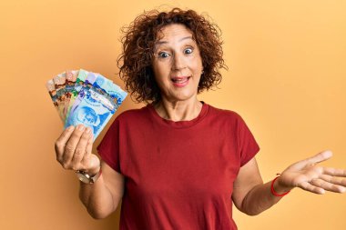 Güzel orta yaşlı olgun bir kadın elinde Kanada doları ile başarıyı mutlu bir gülümsemeyle kutluyor ve kazanan el kaldırarak ifade ediyor. 