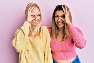 Pembe arka planda yan yana duran iki arkadaş el hareketleriyle gülümsüyor, gözleriyle mutlu yüzlere bakıyor.. 