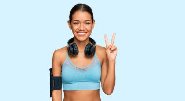 Spor giyim ve kulaklık takan, kameraya gülümseyen ve zafer işareti yapan güzel İspanyol kadın. İki numara.. 