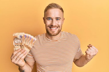 Güney Afrika 'nın 20 rand banknotunu elinde tutan beyaz bir adam gururla bağırıyor, zaferi kutluyor ve kollarını kaldırarak başarıyı kutluyor. 