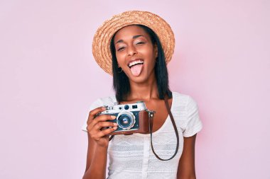 Yazlık şapkalı genç Afro-Amerikan kadın elinde eski model bir kamera, komik bir ifadeyle dilini dışarı çıkartıyor. duygu kavramı. 