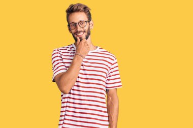 Sakallı, sıradan kıyafetler giyen ve gözlüklü, kameraya kendinden emin, kolları çapraz ve çenesi açık gülümseyen yakışıklı sarışın bir adam. Olumlu düşünmek. 