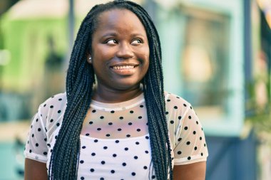 Genç Afrikalı Amerikalı kadın gülümseyerek şehirde mutlu mesut duruyor..