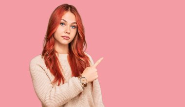 Kış süveteri giyen genç, kızıl saçlı bir kadın elini kaldırmış, ciddi ve sakin bir yüz ifadesi sergiliyor. 