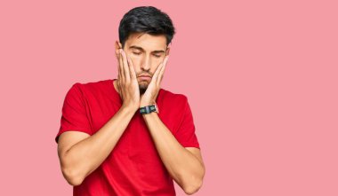 Kırmızı tişört giyen genç yakışıklı adam yorgun eller yüzünü kapatıyor, depresyon ve üzüntü, sorun yüzünden üzgün ve sinirli. 