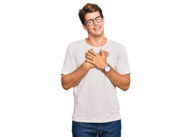 Yakışıklı beyaz bir adam günlük kıyafetler ve gözlük takıyor elleri göğsünde, gözleri kapalı gülümsüyor ve yüzünde minnet ifadesi var. sağlık kavramı. 
