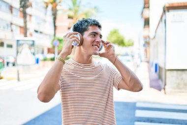 Genç, yakışıklı, beyaz, gülümseyen, müzik dinleyen, kulaklık takan, şehirde yürüyen bir adam..