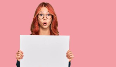 Boş afiş tutan genç kızıl saçlı kadın ağzı açık kalmış, korkmuş ve hayrete düşmüştü. 