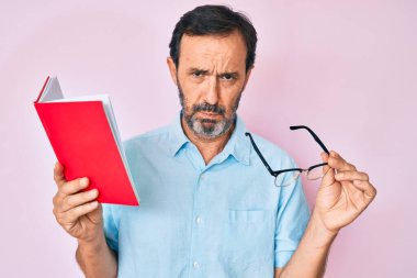 Orta yaşlı İspanyol bir adam elinde gözlük tutarak kitap okuyor. Depresyonda ve endişe içinde, sinirli ve korkmuş bir şekilde ağlıyor. hüzünlü ifade. 