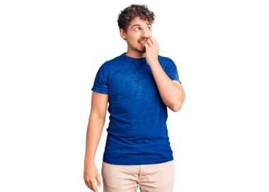 Kıvırcık saçlı, sıradan giyinen, gergin ve gergin görünen elleri ağızda olan, tırnaklarını yiyen genç ve yakışıklı bir adam. anksiyete. 