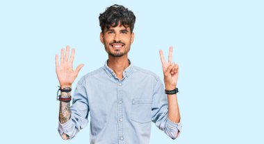 Gündelik kıyafetler giyen genç İspanyol adam yedi numarayı gösterip işaret ederken kendinden emin ve mutlu bir şekilde gülümsüyor.. 